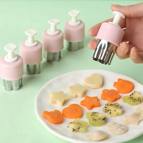 Eine Hand hält ein Set aus pinkem Silikon-Formen für Obst und Gemüse, wie Herzen und Sterne, auf einem weißen Teller.