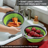 A green silicone folding drain basket holding carrots and strawberries in a kitchen sink.