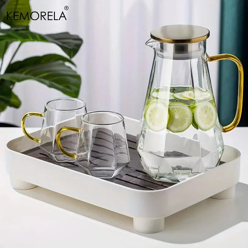 A glass pitcher set featuring a clear glass teapot and two glasses with gold accents, placed on a white tray.