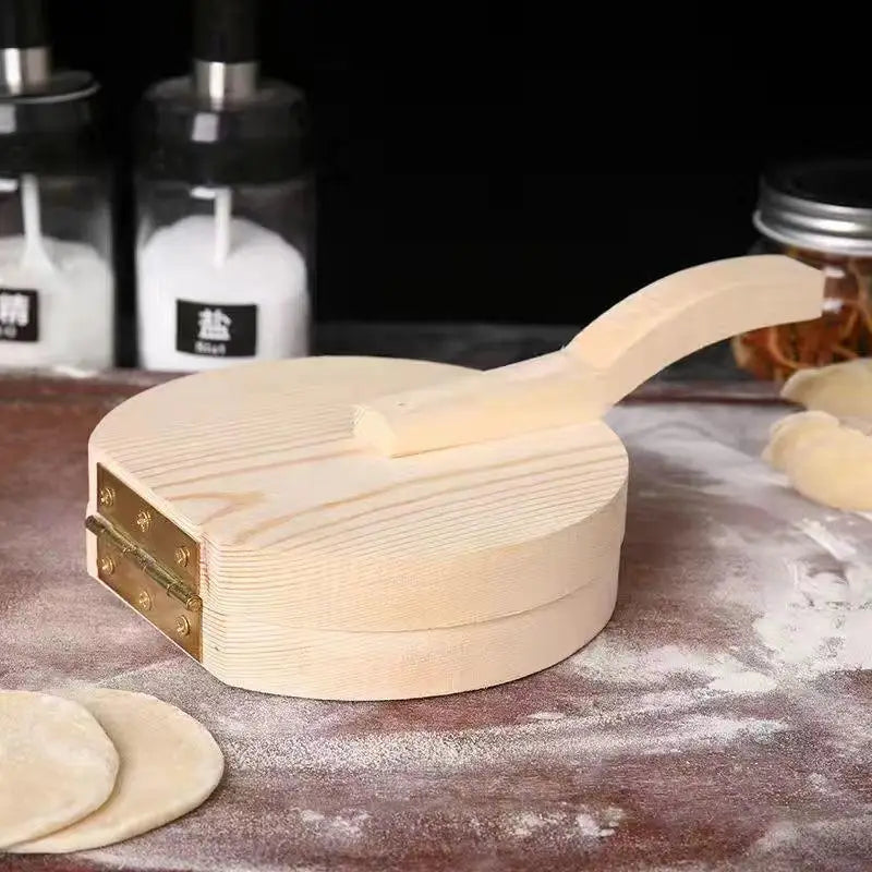 A light wood dumpling press tool rests on a dark surface with some dough pieces nearby.