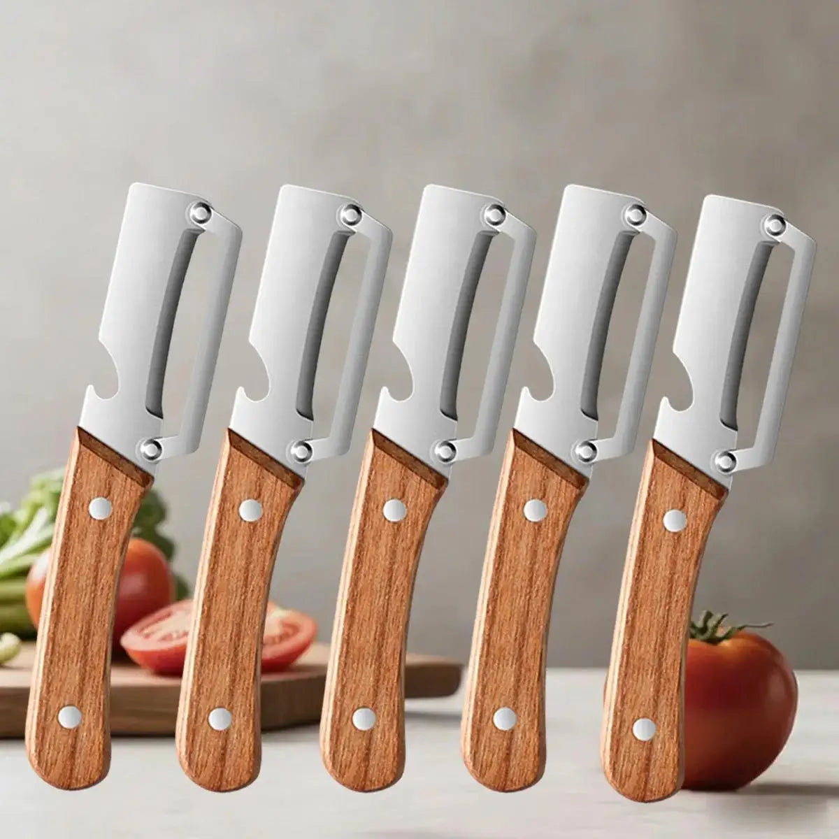 Five stainless steel peelers with wooden handles are displayed next to fresh produce.