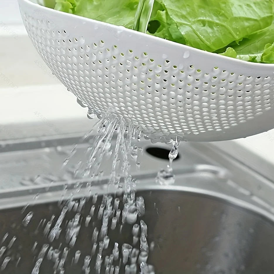 A white multi-purpose kitchen strainer is pouring water over green lettuce into a metal sink.