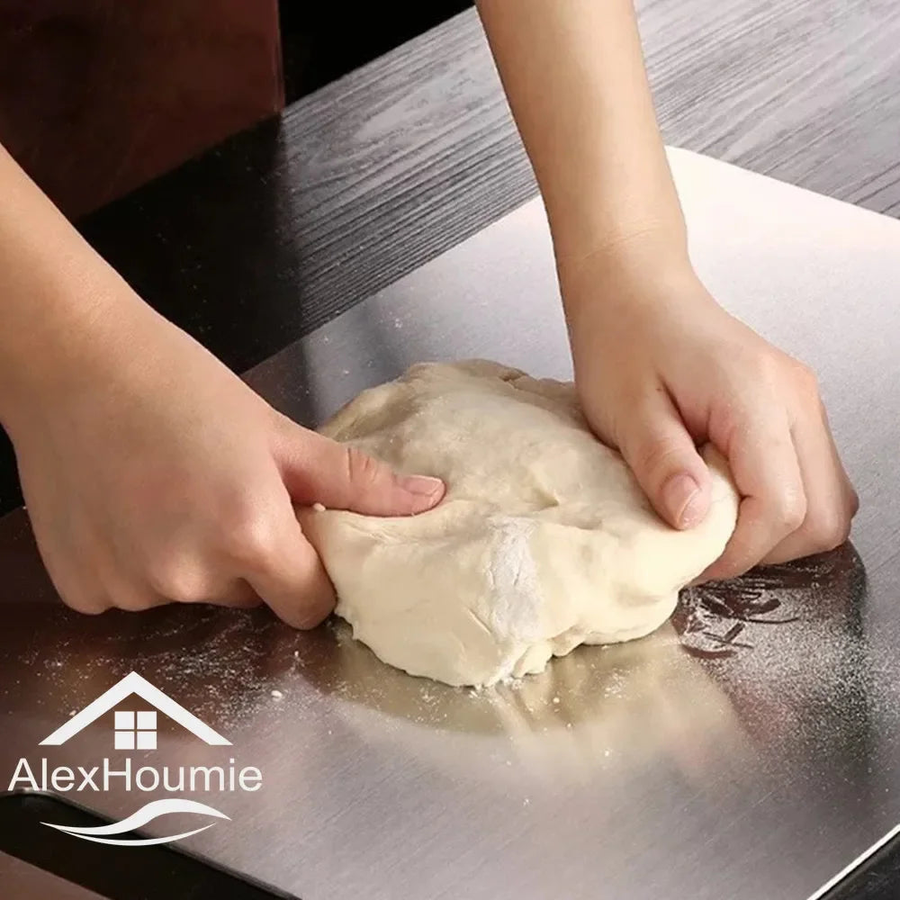 Hands are pressing dough onto a stainless steel cutting board for kitchen preparation.