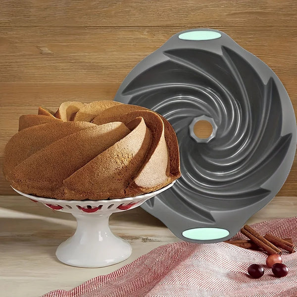 A gray silicone cyclone cake mold sits on a white pedestal dish next to a red cloth and cinnamon sticks.