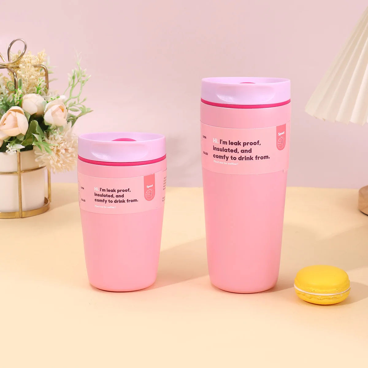 A pink insulated vacuum coffee mug is displayed on a light surface next to a yellow object.