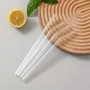A clear glass straw set with five straws rests on a wooden cutting board next to a slice of lemon.