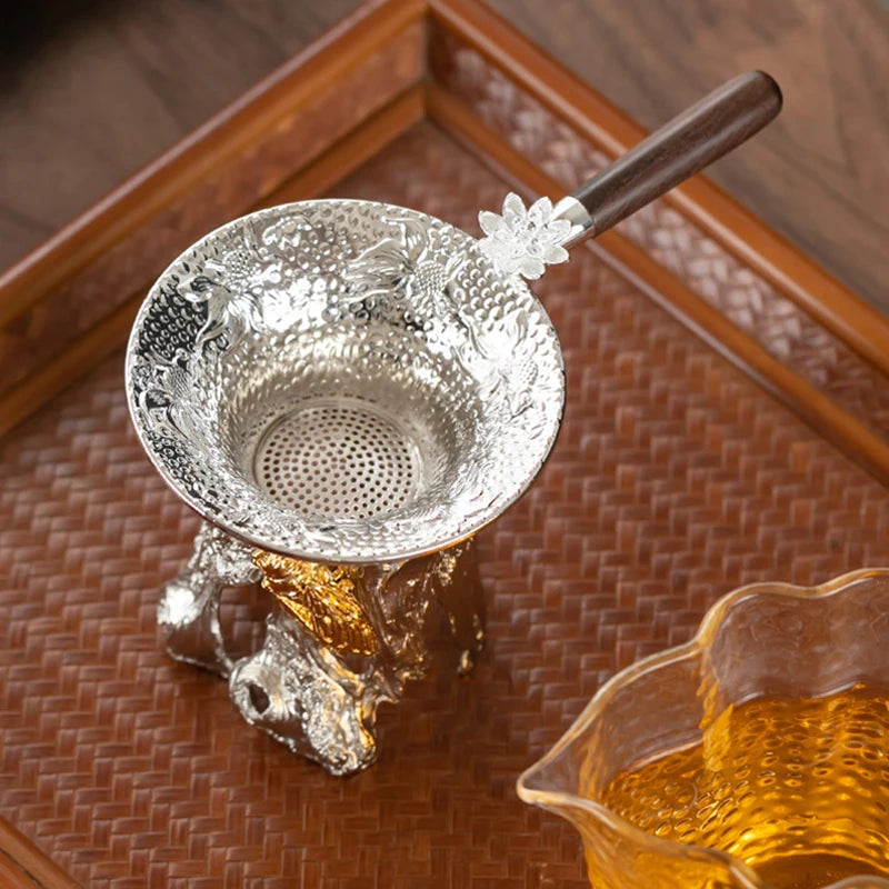 A stainless steel tea strainer filter is shown resting on a wooden tray with an amber liquid nearby.