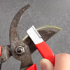 A hand holds a professional multi-material knife sharpener with a red handle and a silver blade, set against a gray backgroun