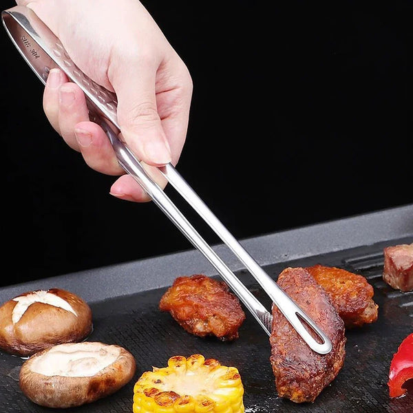 Eine Hand hält professionelle Edelstahl-BBQ-Zangen, die zum Grillen oder Servieren von Speisen verwendet werden.