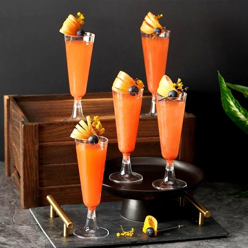 A display of bright orange cocktails in clear disposable champagne flutes set on a wooden tray.