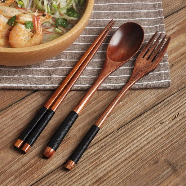 Set aus natürlichem Holzbesteck, einschließlich Chopsticks, Löffel und Gabel, auf einem gestreiften Servietten neben einer Sc