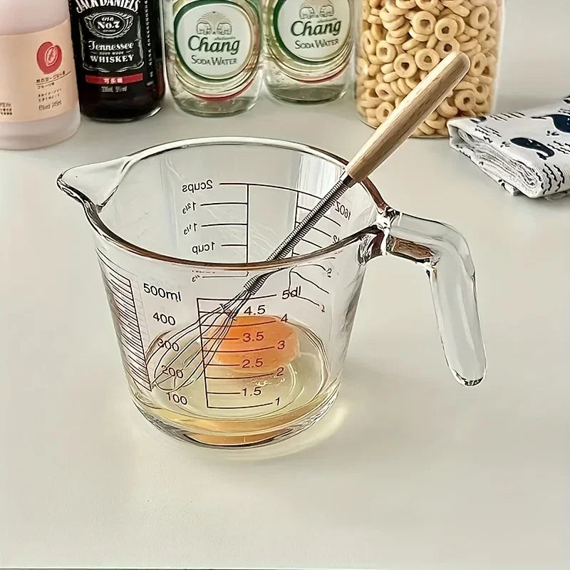 Una jarra de vidrio con líquido y un batidor de madera, con botellas de licor al fondo.