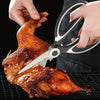 Hands are using heavy duty stainless steel kitchen scissors to cut a roasted chicken on a grill grate.