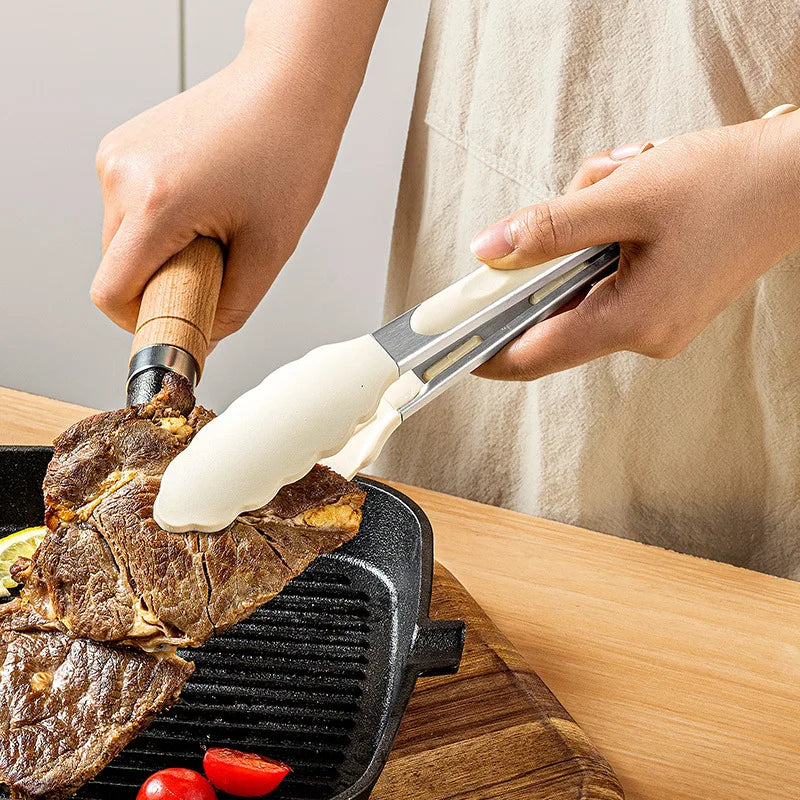 Hands use heavy-duty silicone kitchen tongs to flip grilled meat on a black grill pan.