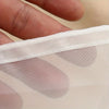 A close-up of a translucent mesh filter bag with light pink polka dots being held by a hand.