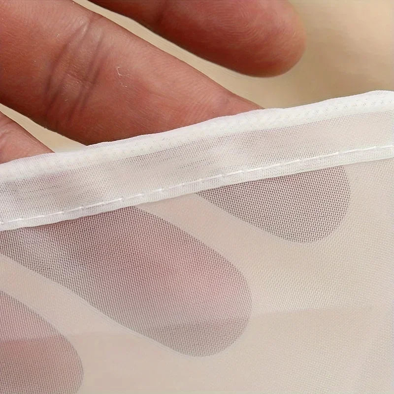 A close-up of a translucent mesh filter bag with light pink polka dots being held by a hand.