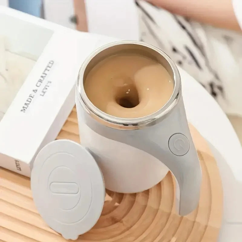 A silver automatic self-stirring mug filled with light brown liquid sits on a wooden surface.