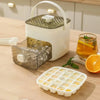 A white reusable grid ice cube mold set with a lid and a clear ice cube tray is displayed on a wooden table.