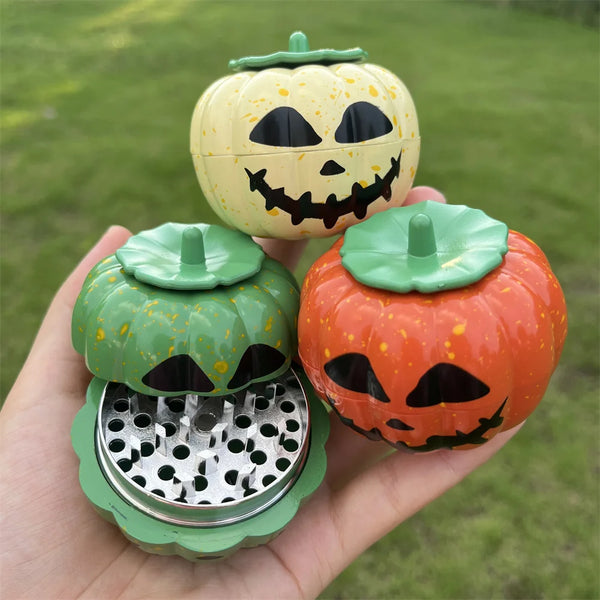A hand holds an orange pumpkin-shaped manual herb and spice grinder with a carved face.