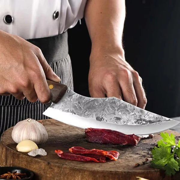 Eine Hand benutzt ein Edelstahlkochmesser, um rohes Fleisch auf einem Holzbrett zu schneiden.