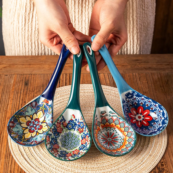 Eine Hand hält ein Set aus blauen und grünen Keramikschöpflöffeln auf einer geflochtenen Matte.