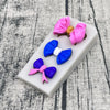 A set of silicone baking molds shaped like bows in pink and blue colors resting on a white rectangular tray.