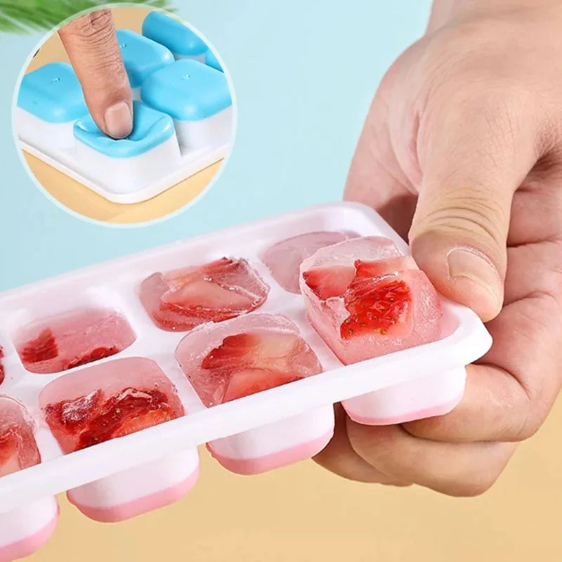 A hand holds a pink silicone ice cube mold set with a lid, showing several red fruit-flavored ice cubes.