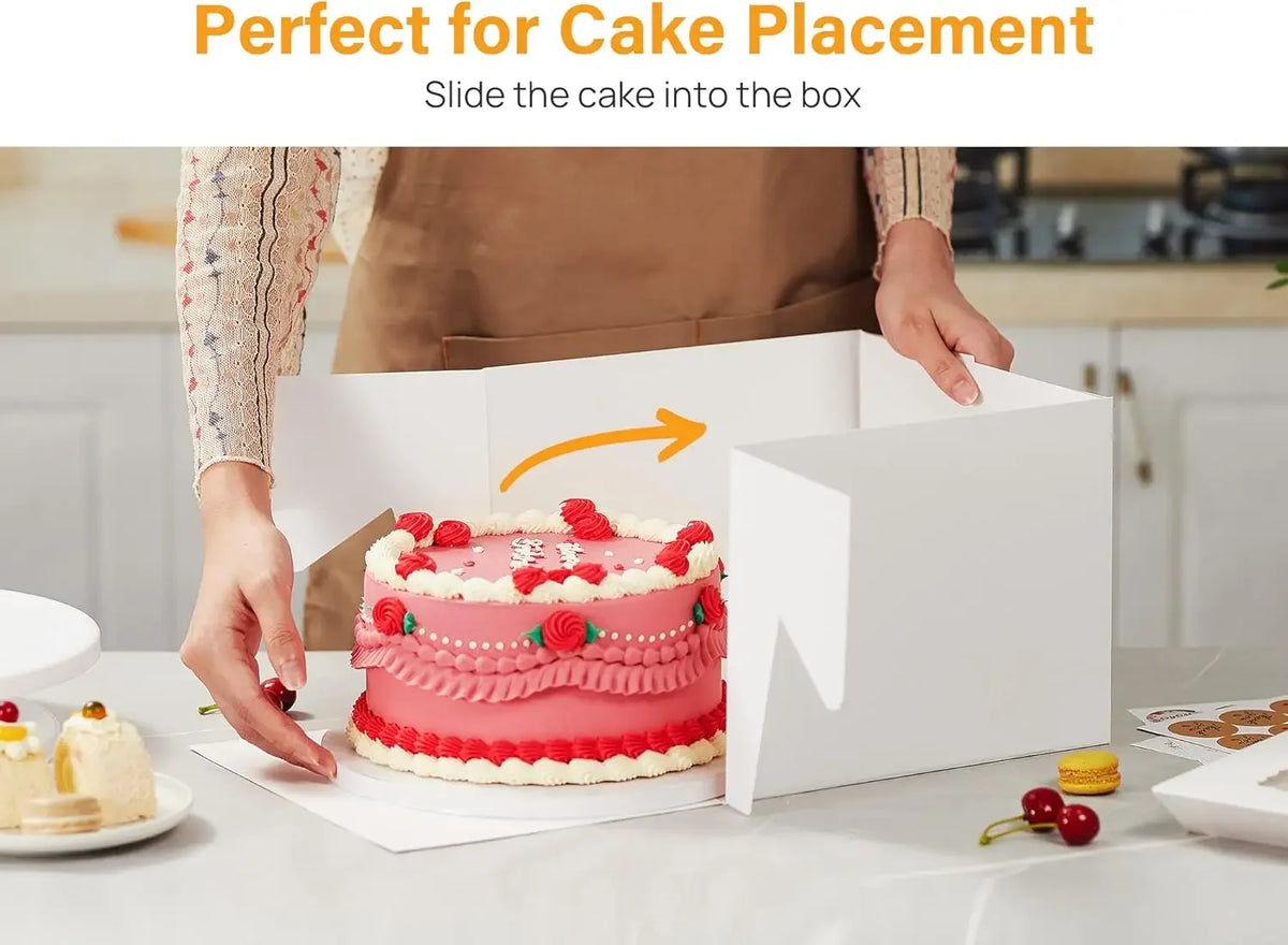 A hand slides a pink decorated cake into a white square window box for cake placement.