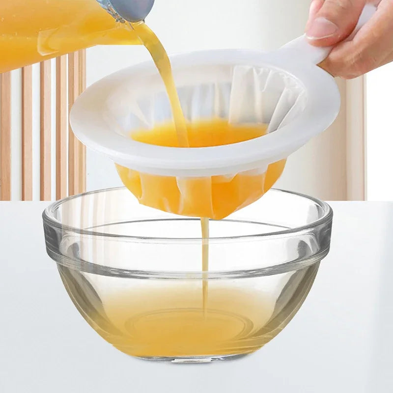 A hand pours orange juice through a multi-mesh fine strainer into a glass bowl.