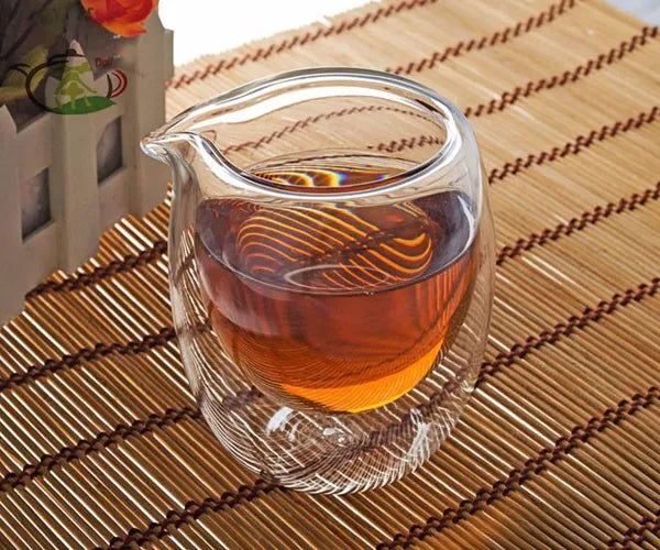 A clear glass teapot or pitcher filled with amber tea is resting on a bamboo mat.
