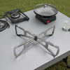 A foldable stainless steel steaming rack is placed on a table next to a portable gas burner.