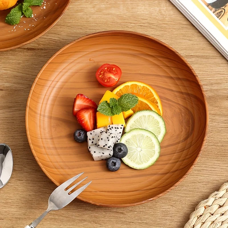 A wooden plate features fresh fruit like strawberries, oranges, and lime slices, served on a light brown wooden surface.