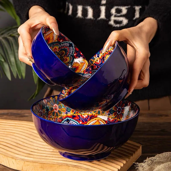 Eine Hand hält eine tiefblaue Keramik-Reisschale mit bunten Mustern, die auf einer Holzoberfläche liegt.