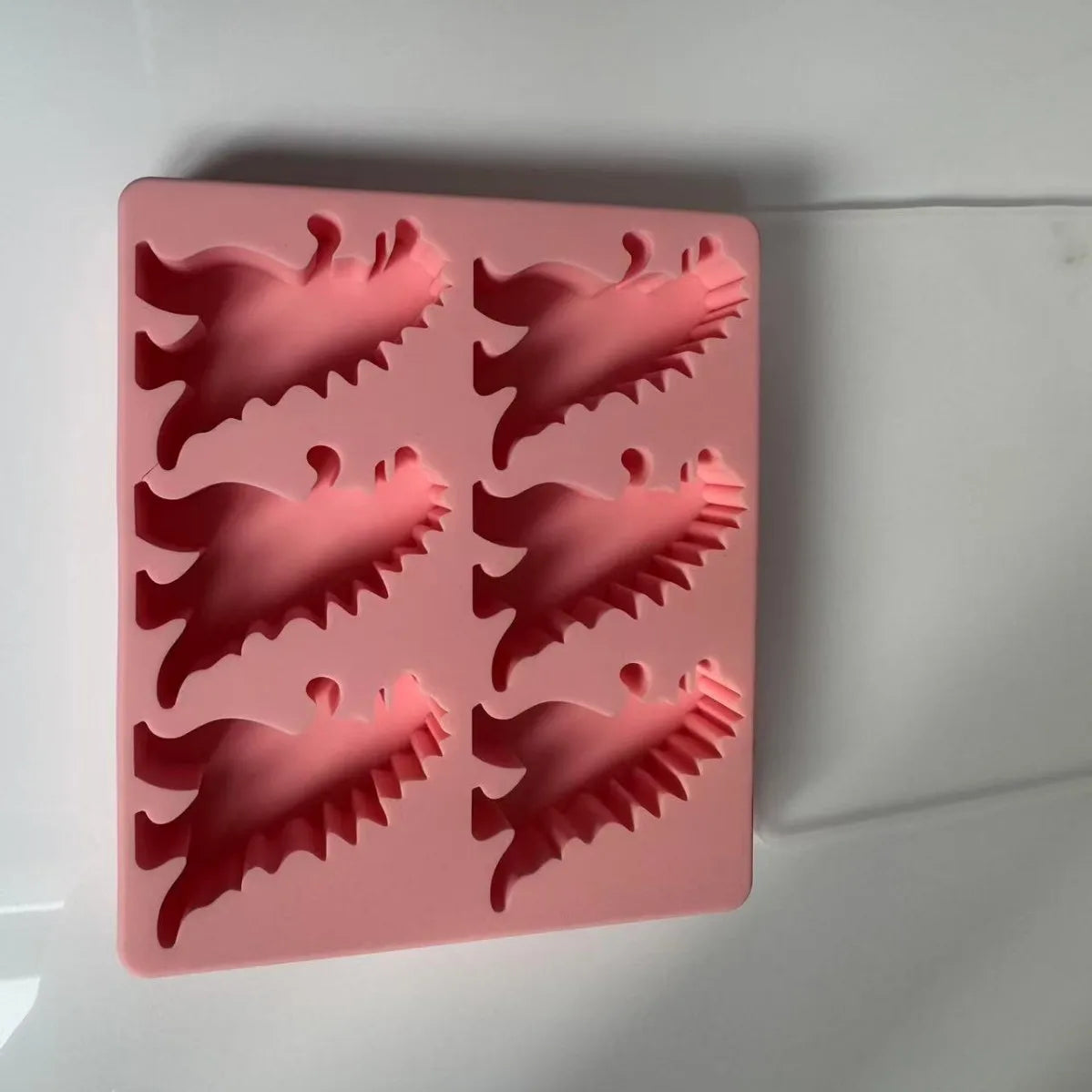 A pink silicone dinosaur ice cube tray set with various dinosaur shapes.