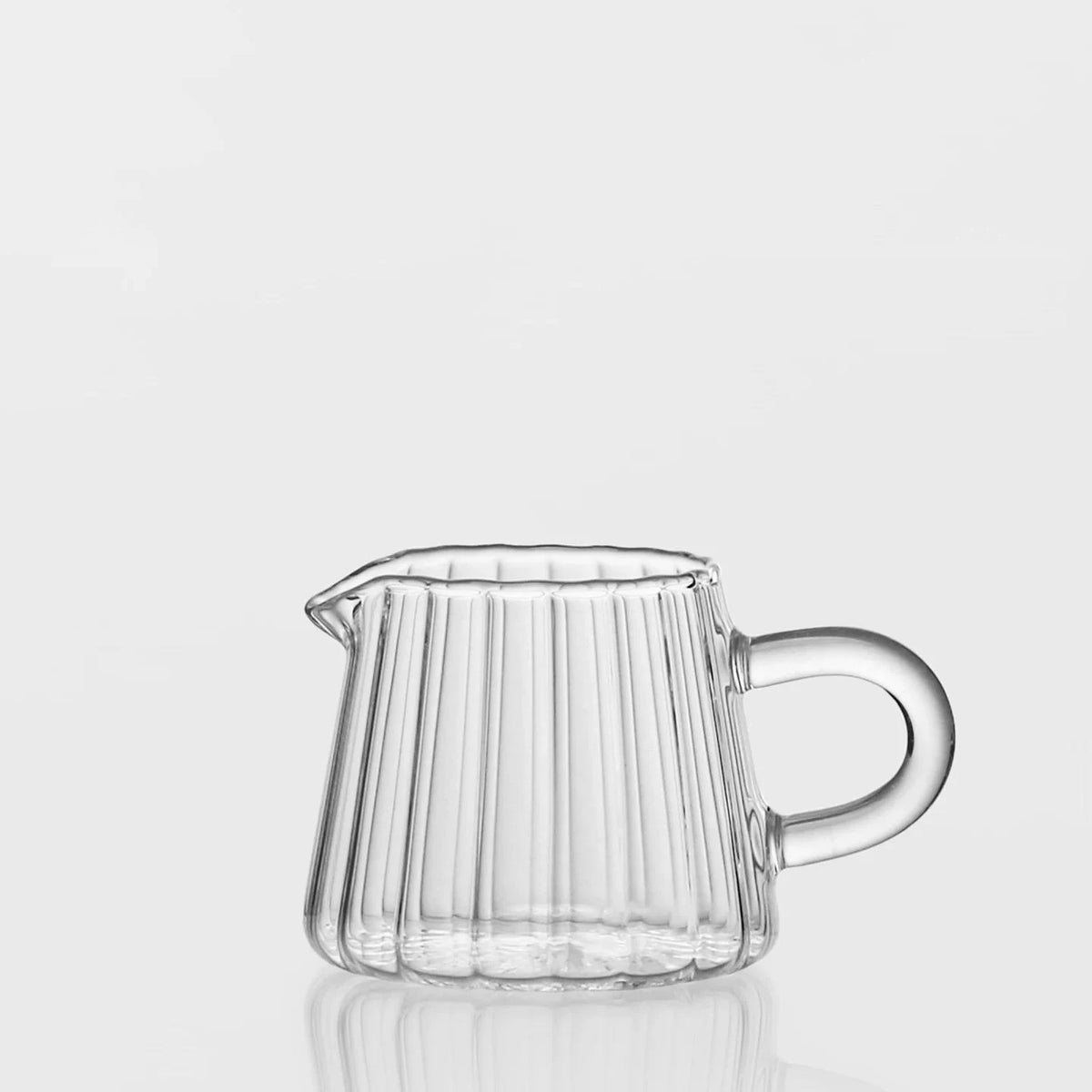 A clear striped borosilicate glass milk pitcher with an ergonomic handle.