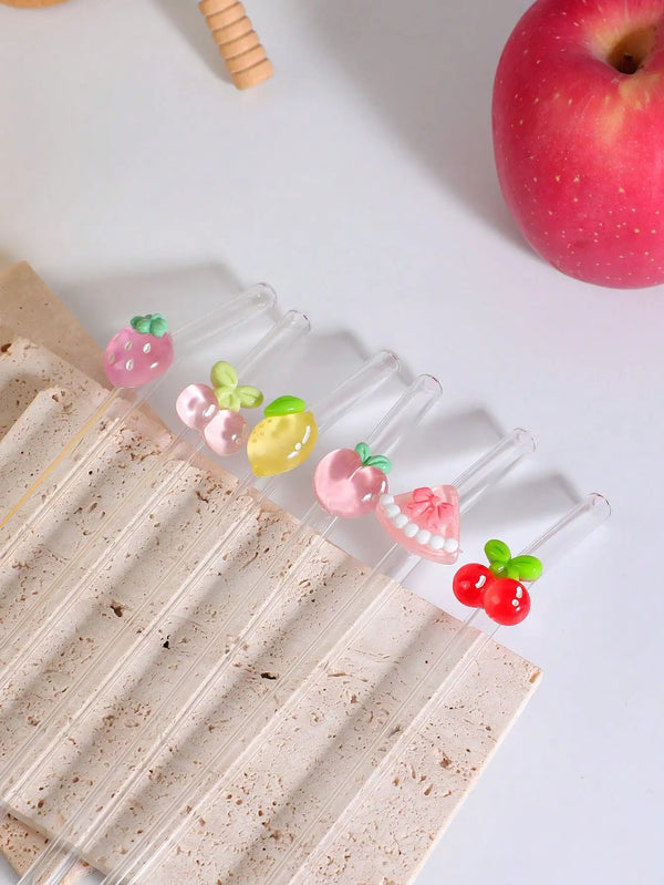 Set hitzebeständige Glasstroh in Früchtenform, darunter Erdbeeren und Äpfel, auf helbem Braun