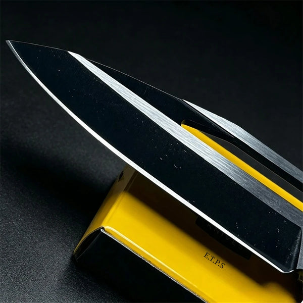 A folding knife with a black blade and silver edge is shown resting on a yellow handle.