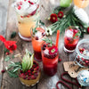 A collection of reusable plastic drinking straws and various beverages, including cocktails and juices, arranged on a wooden 