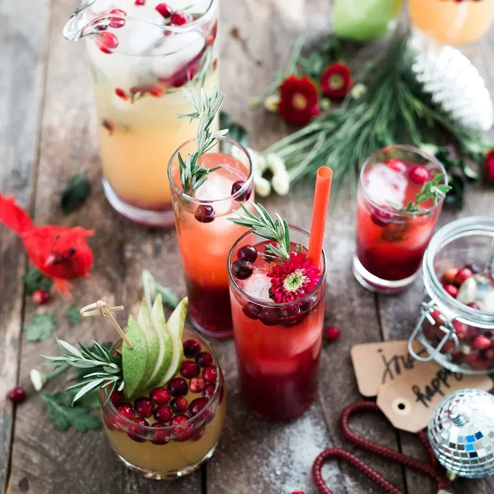 A collection of reusable plastic drinking straws and various beverages, including cocktails and juices, arranged on a wooden 