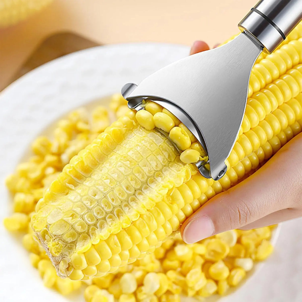 A hand is using a stainless steel corn planer to peel corn kernels from the cob.