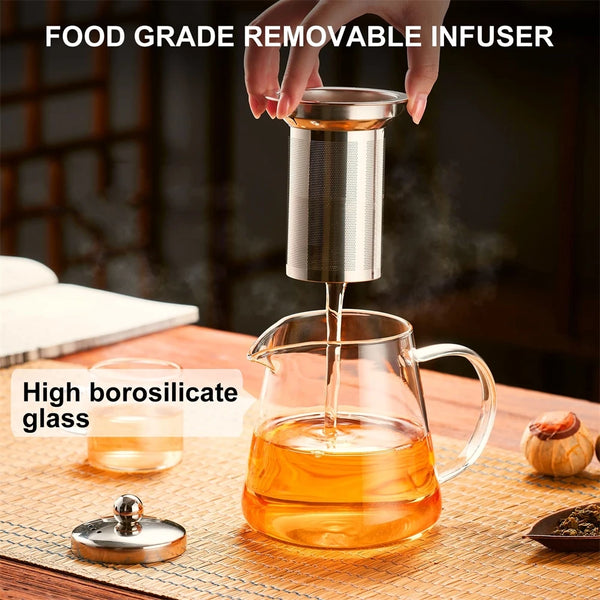Eine Hand gießt Flüssigkeit in eine Glasteekanne mit einem rostfreien, wiederverwendbaren Teeinfuser.