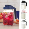 Jarra de vidrio para jugos y bebidas con líquidos de varios colores, incluyendo rosa y rojo, en un vaso transparente