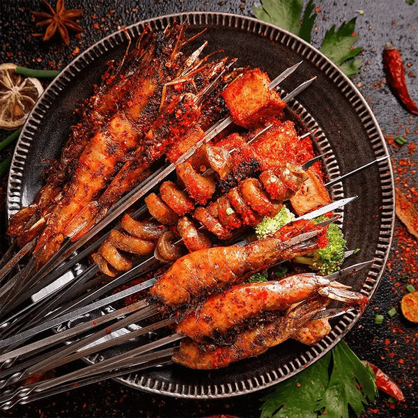 Teller mit gegrillten Meeresfrüchte-Spießen auf Metallspießen, gewürzt mit Chili und garniert mit grünen Kräutern.