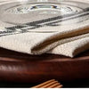 A stack of light-colored cloth napkins rests on a dark wooden trivet.