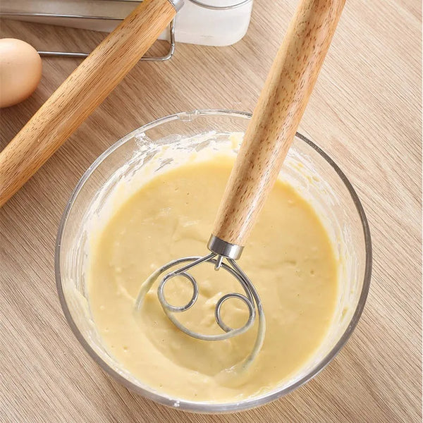 Edelstahl- und Holz-Teigschneebesen mischen einen hellgelben Teig in einer Glasschüssel.