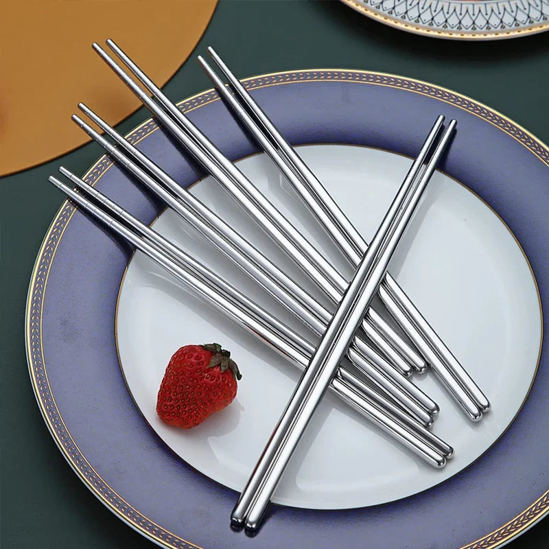 A set of silver stainless steel chopsticks resting on a white plate with a gold rim.