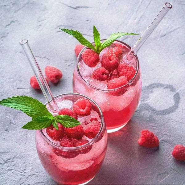A glass of pink raspberry smoothie garnished with mint and served in a reusable glass with a straw.