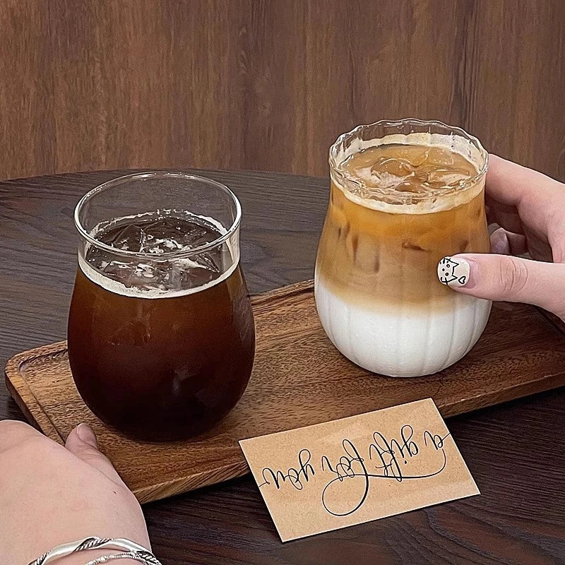 A glass of iced coffee or tea is presented in an elegant transparent glass tumbler on a wooden board.