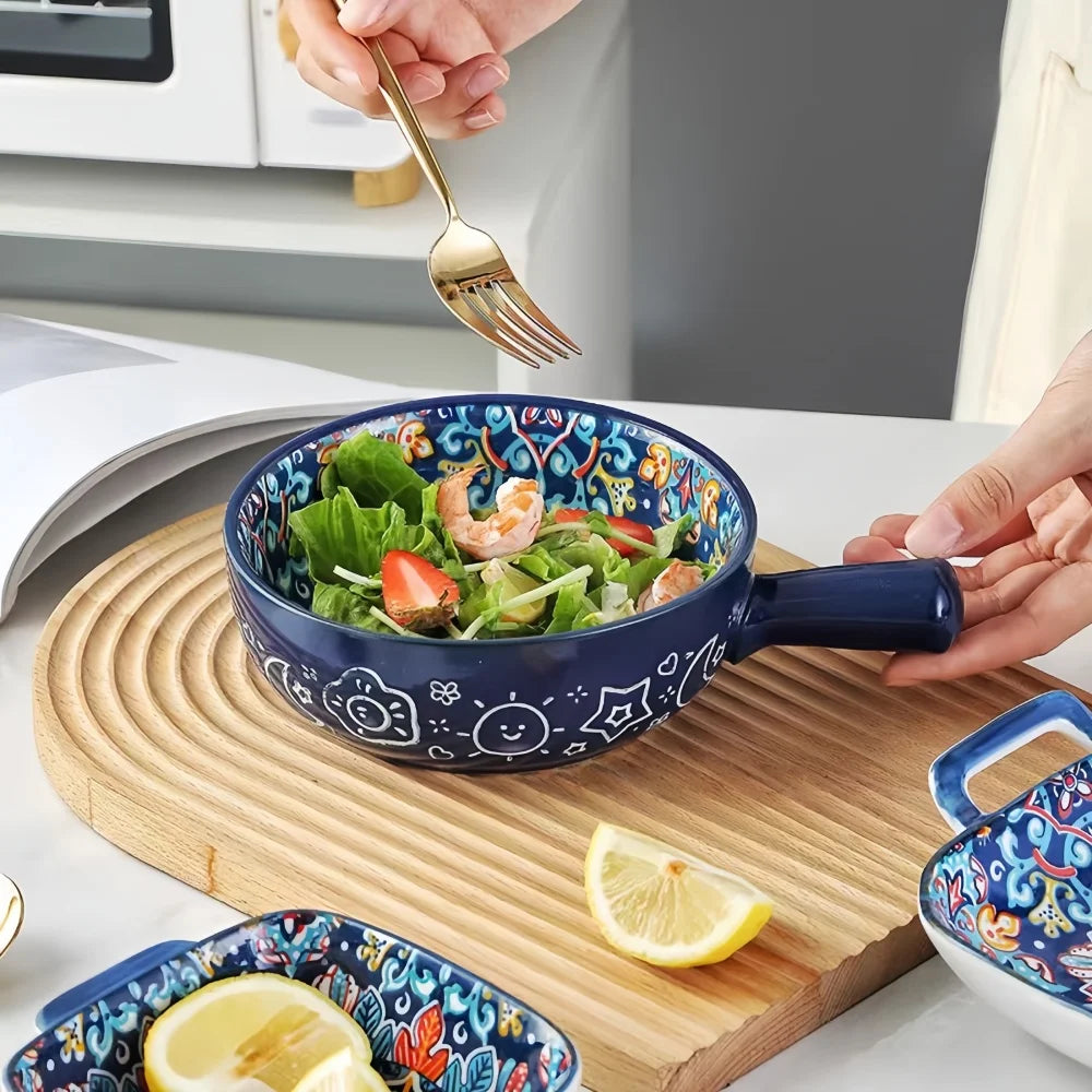A hand-painted ceramic salad bowl with a handle filled with green salad and garnished with salmon and strawberries on a woode