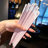 A hand holds a set of pink and white reusable Japanese Chinese chopsticks.